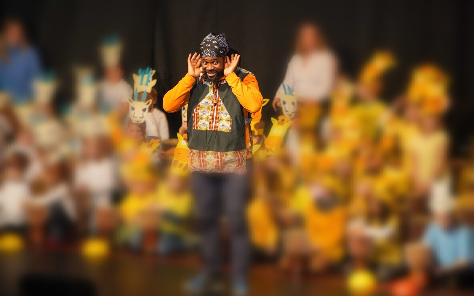 Trommellöwe Baba macht eine "große Ohren Geste" bei einem Trommelprojekt in der Schule